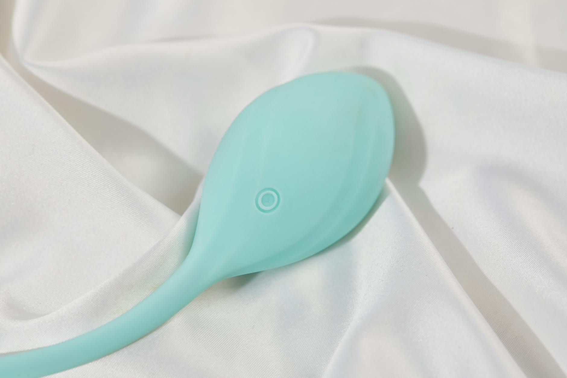 A sleek teal clitoral vibrator on white silk, representing modern shared intimacy.