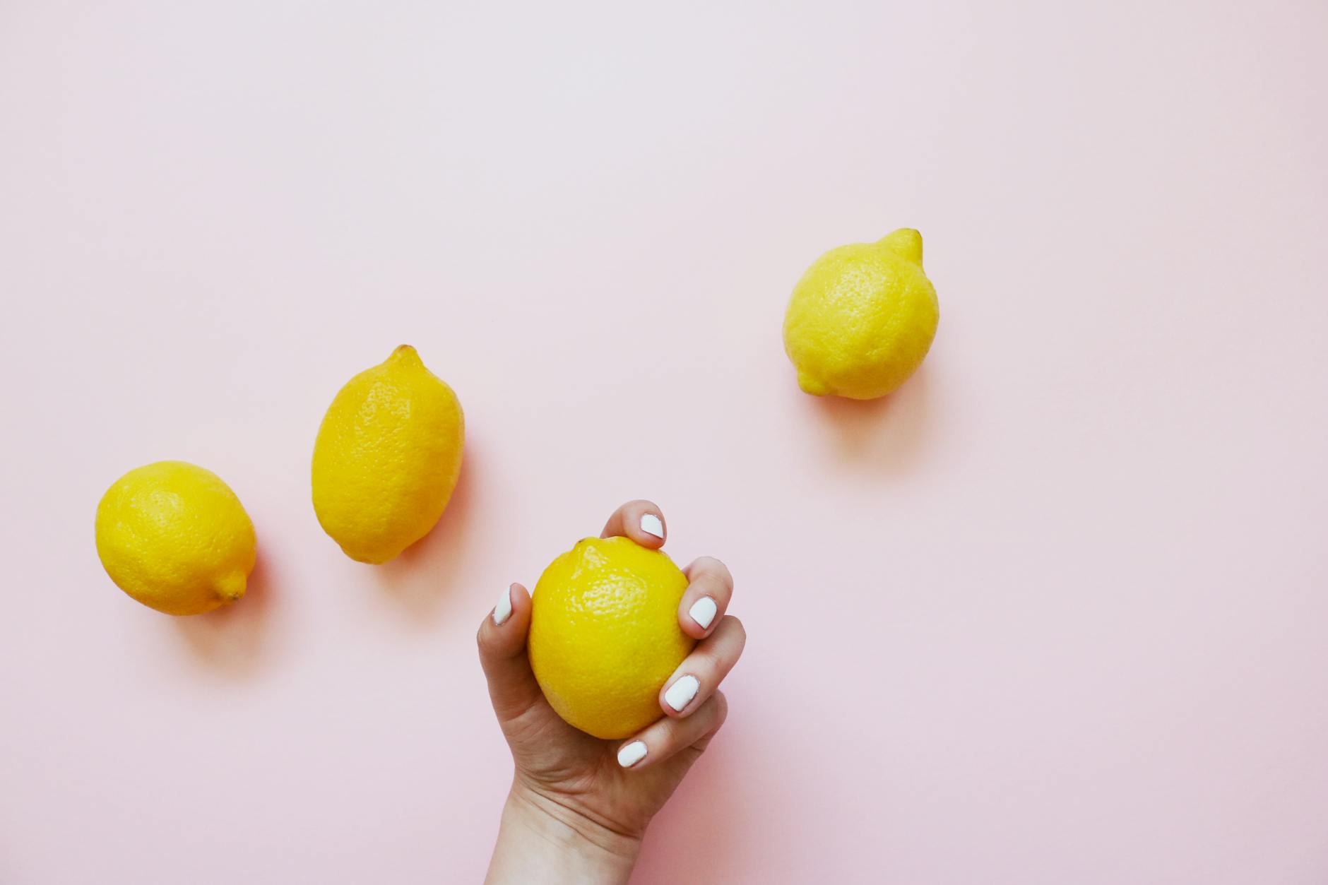 A hand holding a lemon on soft pink background, symbolizing refreshed sensation and pleasure