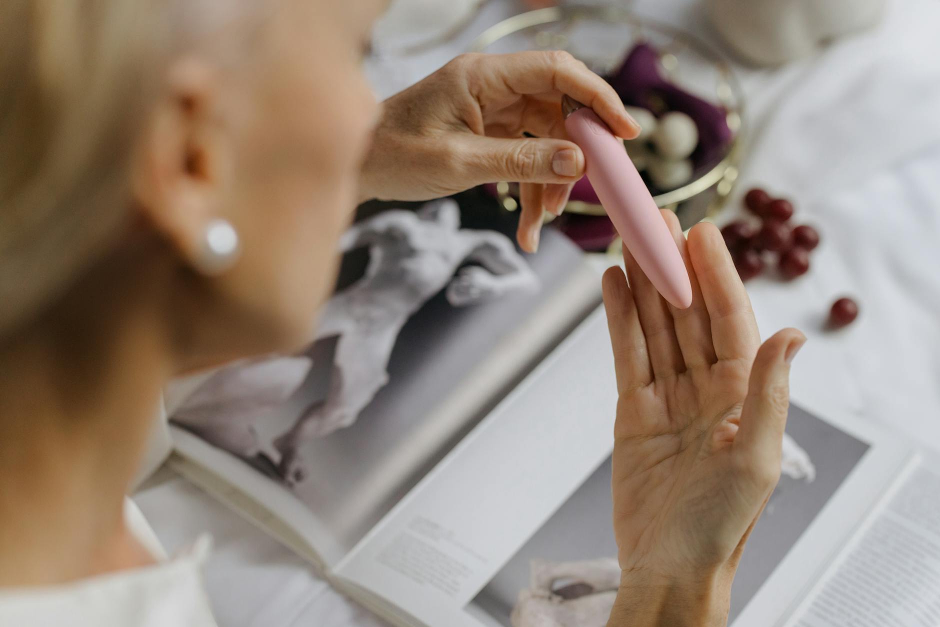 Close-up of a woman holding a pink vibrator with art books nearby, emphasizing personal wellness and intimate recovery