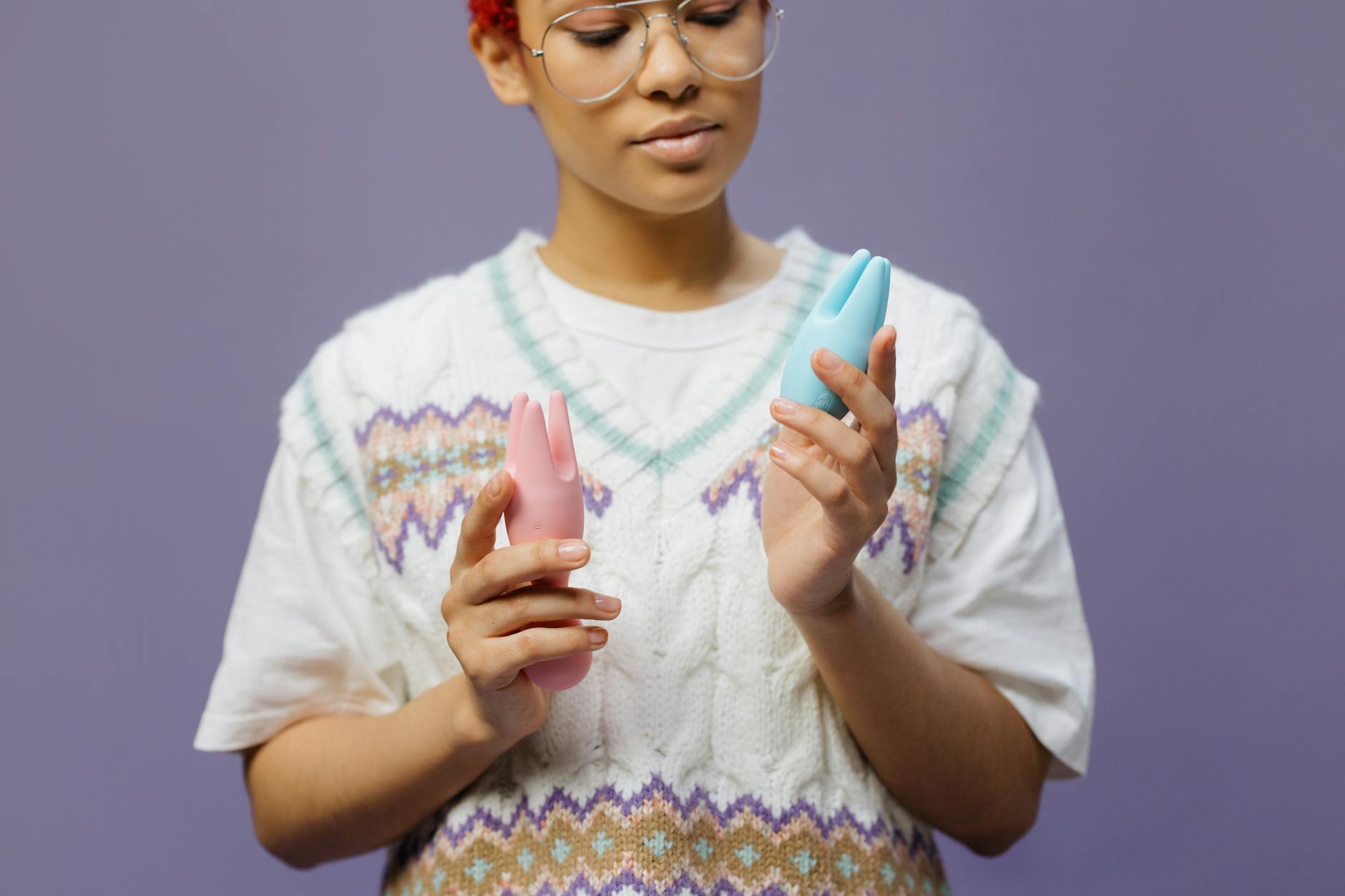 Woman holding blue and pink silicone clitoral vibrators in contemplative pose